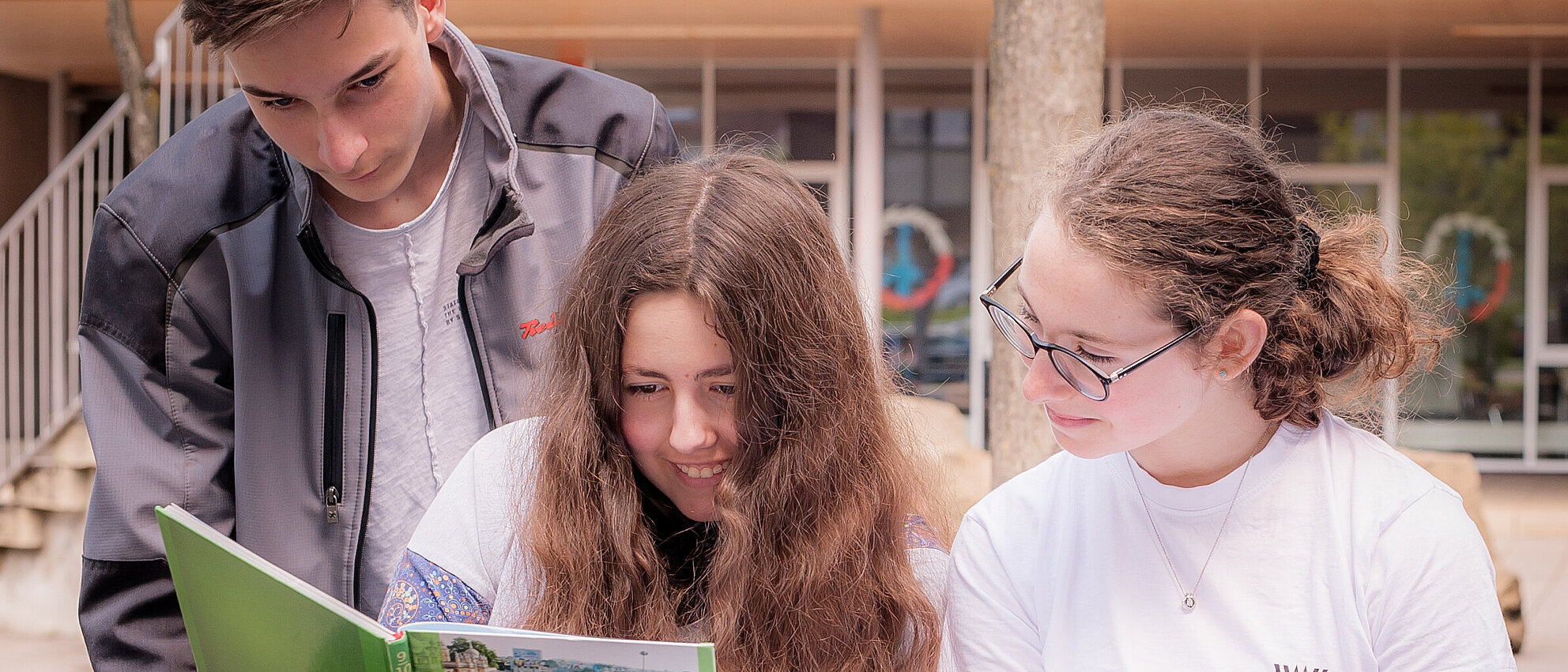 Ein Schüler und zwei Schülerinnen schauen gemeinsam in ein Buch und lernen.